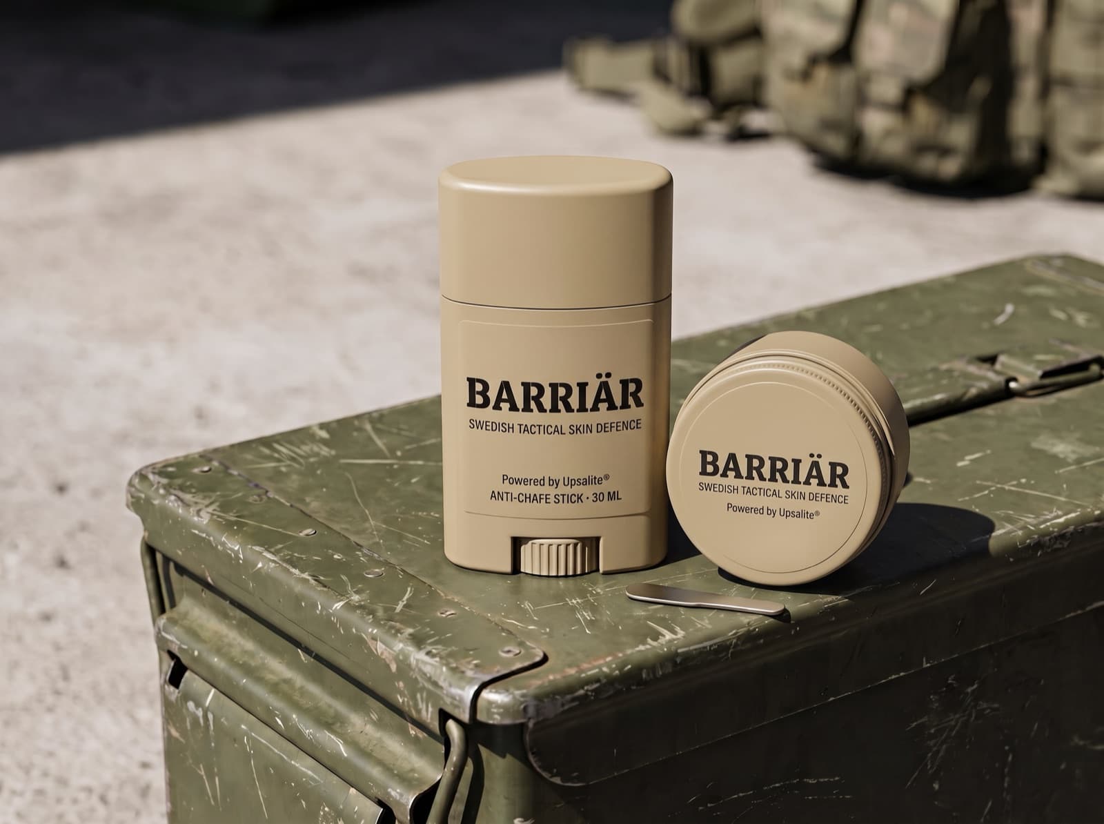 Barriär anti-chafe stick and jar in matte sand-beige packaging on a scratched olive-green ammunition box in hard sunlight, both printed with the Barriär wordmark in Bitter slab-serif over Swedish Tactical Skin Defence